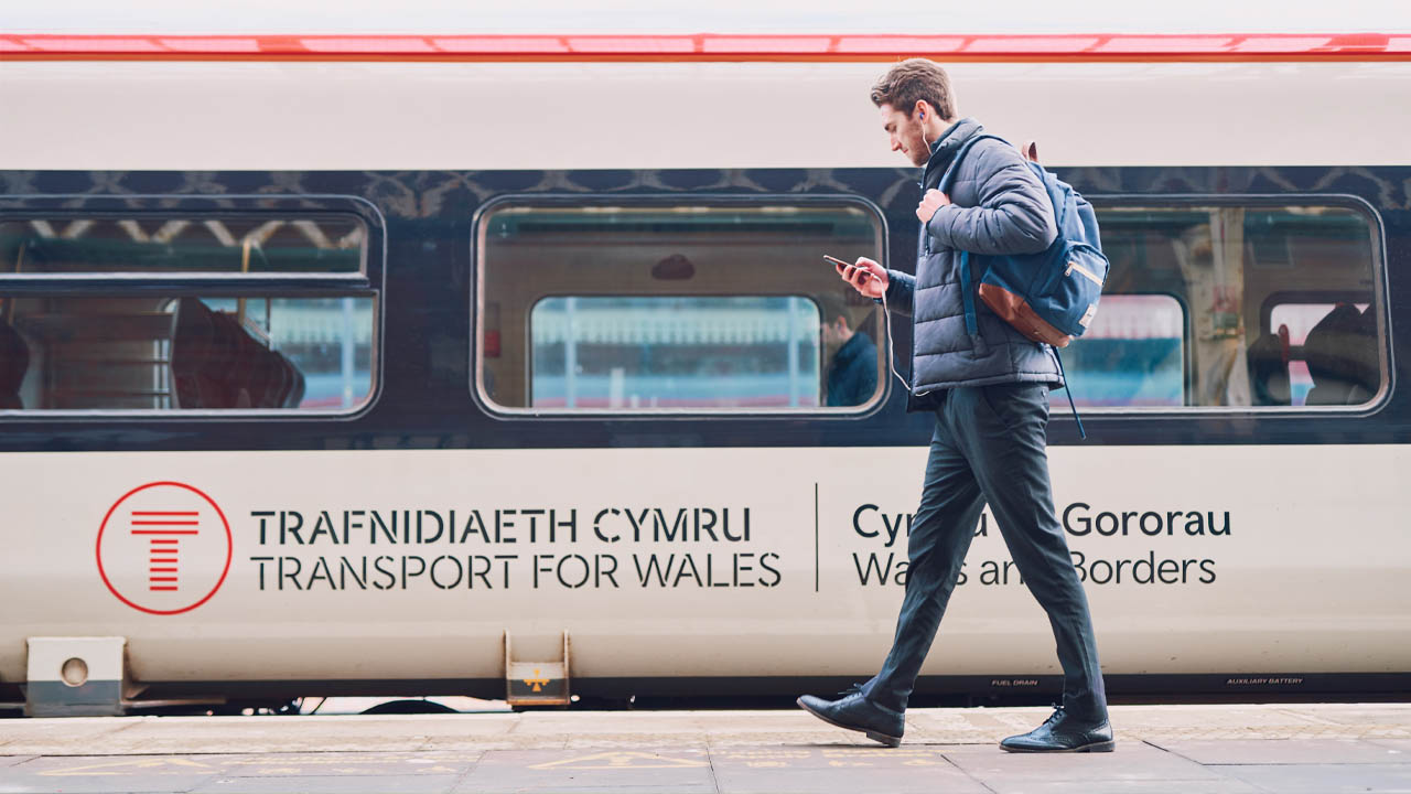 A man walking past a TfW train whilst looking at his phone